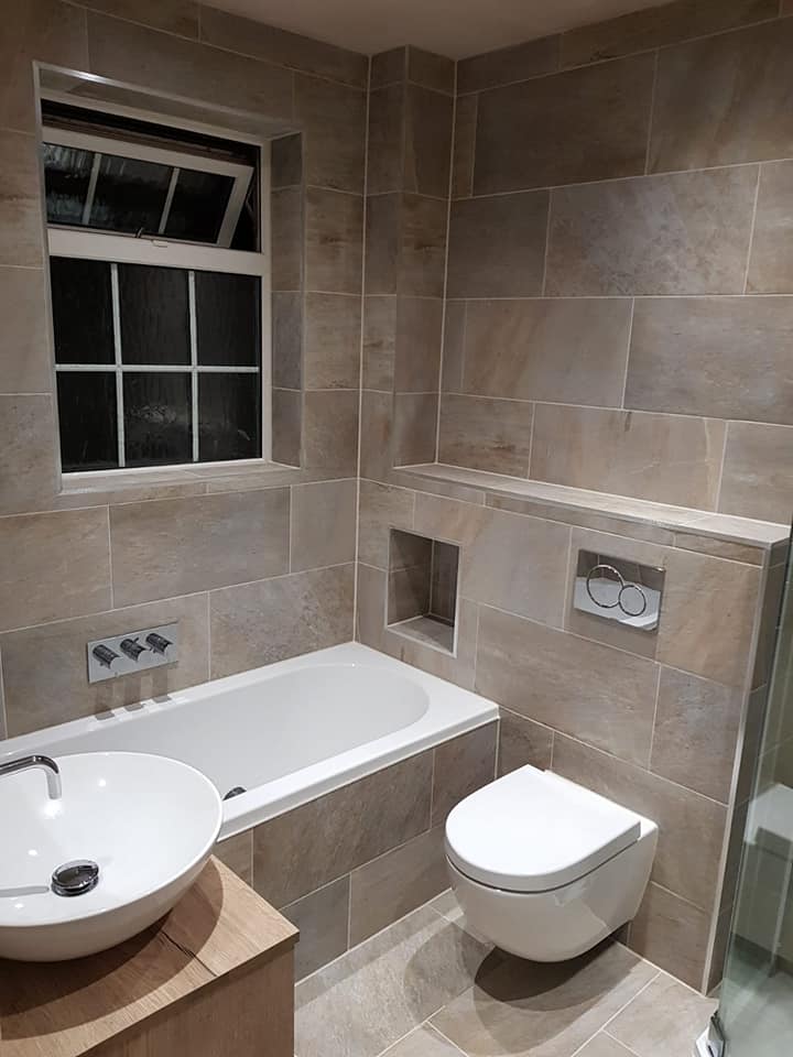 Compact stone-tile bathroom with wall-hung WC, bath and recessed niche