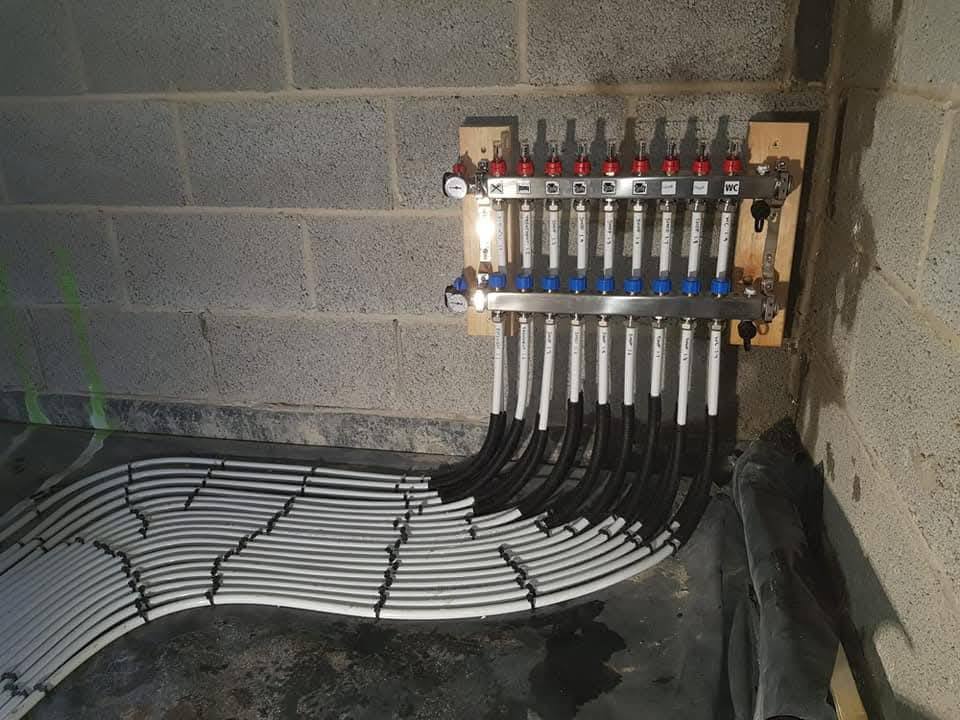 Wall-mounted 10-zone underfloor heating manifold with red and blue actuators, labelled per room